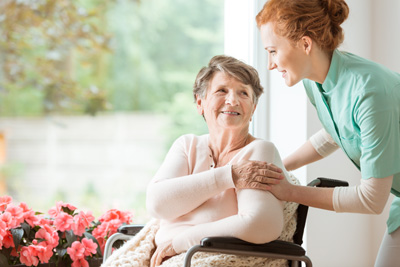 An elderly woman is sitting in a wheelchair and is being comforted by a smiling nurse